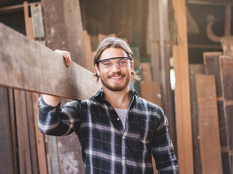 Mandlig tømrer med træ på skulderen