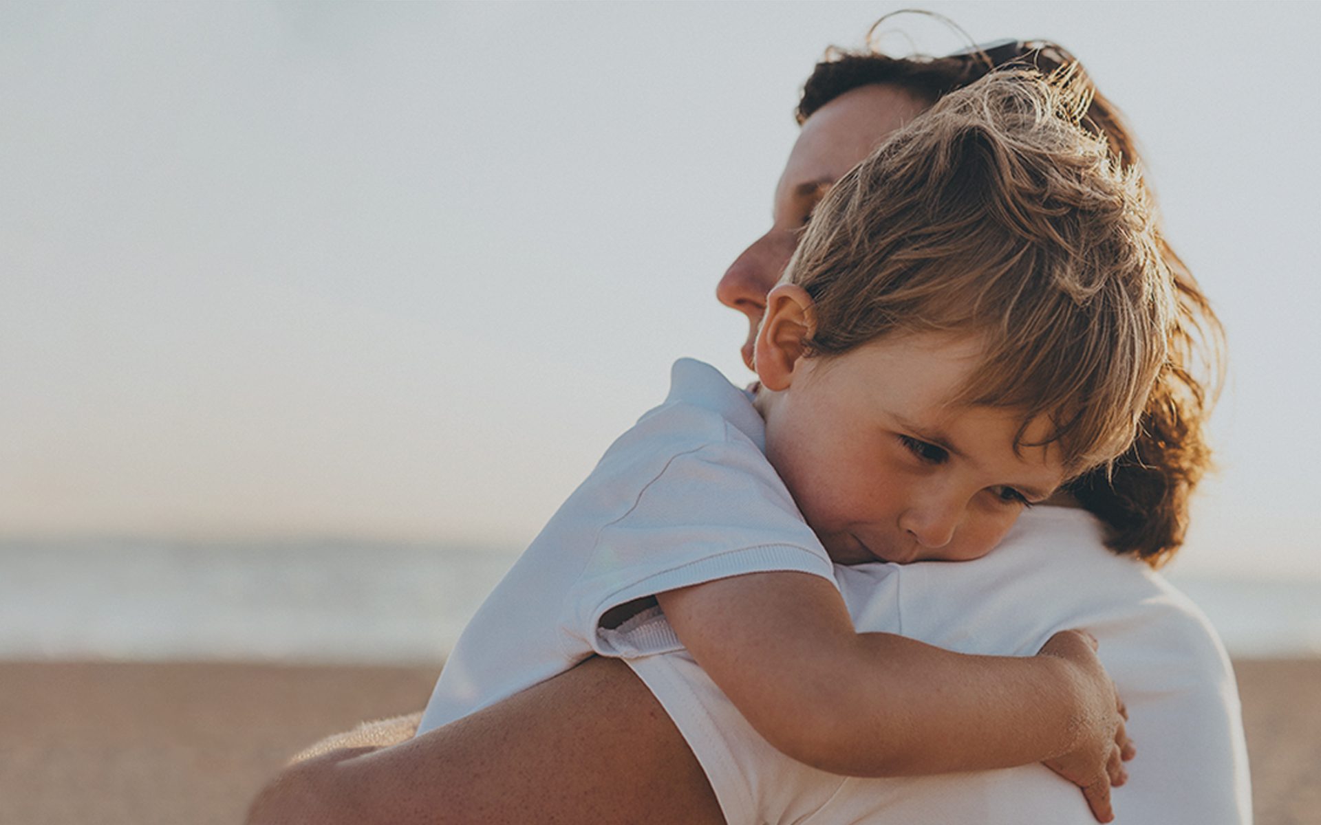 Kvinde krammer dreng på stranden