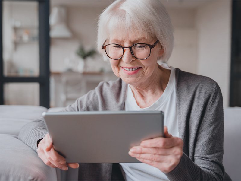 Ældre dame sidder i sofaen med iPad