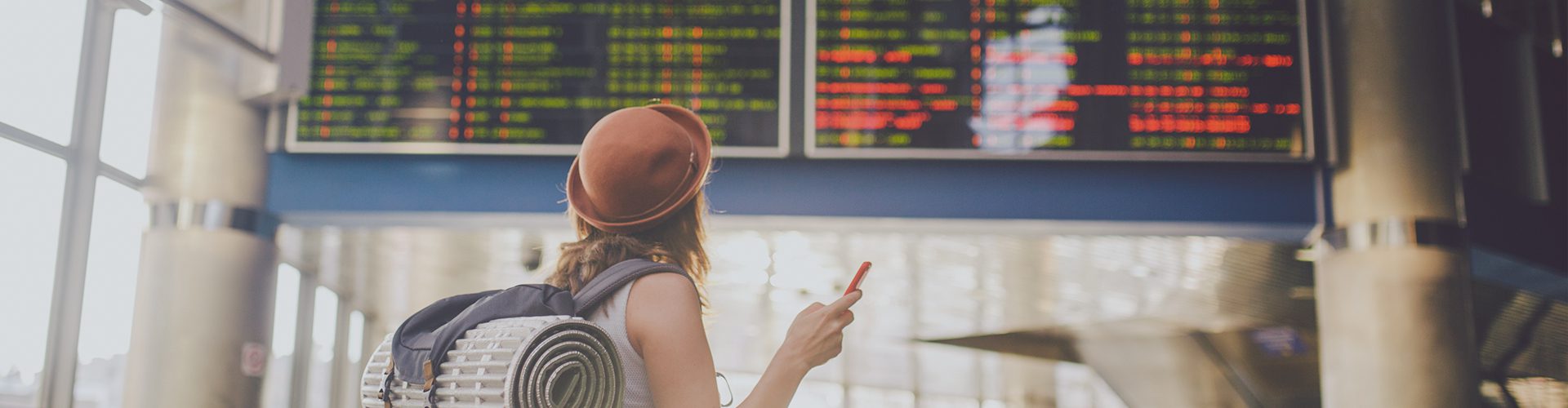 Kvinde står i lufthavnen med telefon og kigger på afgangsskærm