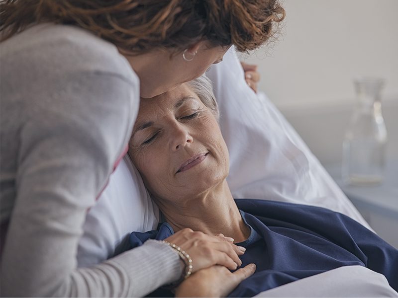 Kvinde kysser ældre kvinde på panden i sygesengen