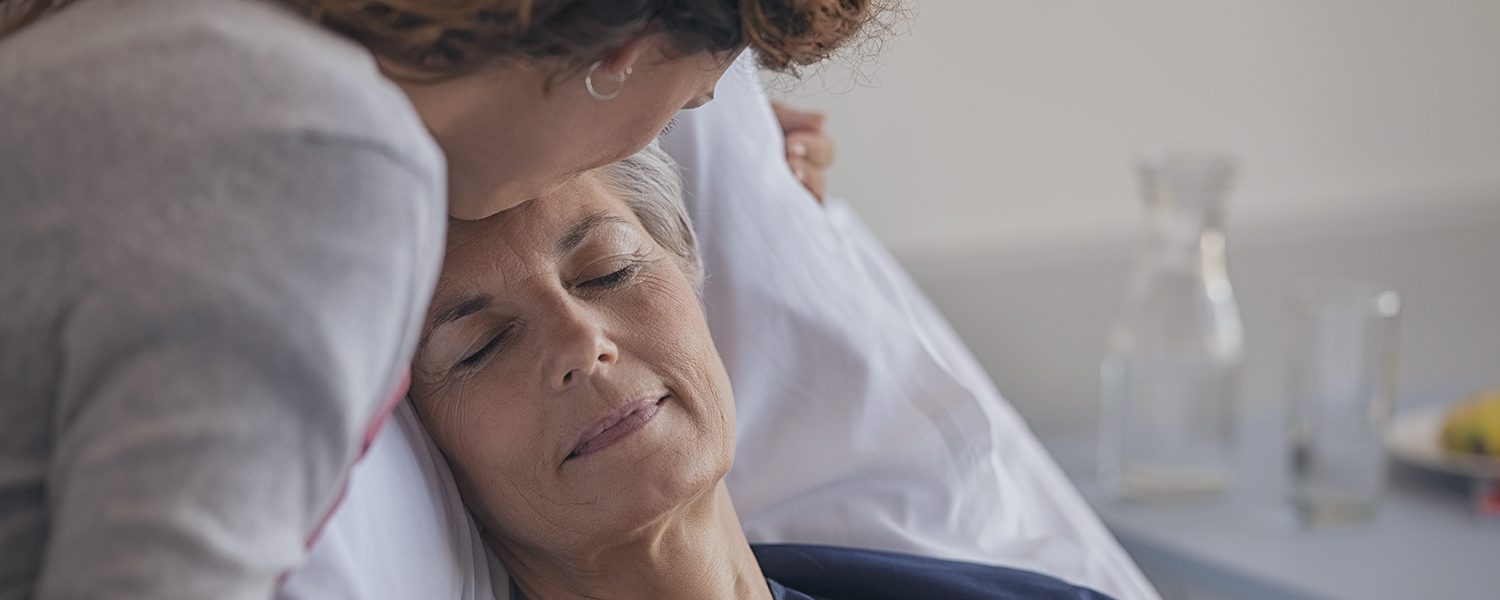 Kvinde kysser ældre kvinde på panden i sygesengen