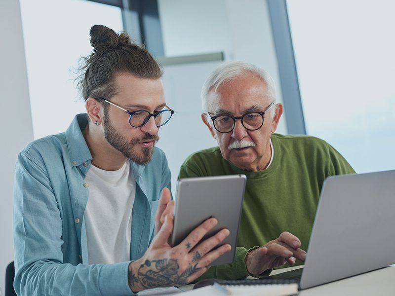 Ung og ældre mand sidder med computer og tablet