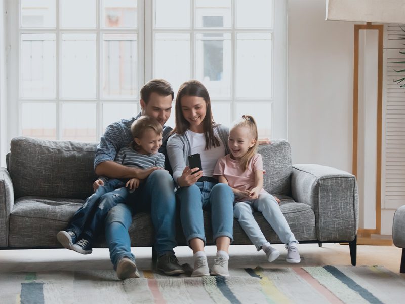 Mor og far med datter og søn kigger på telefon i sofa